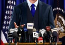 Trump Targets BBC: Media Manipulation Exposed A speaker at a press conference with multiple microphones in front of them