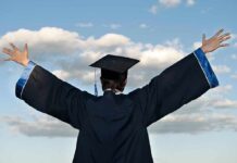 Graduate in cap and gown with arms raised against a blue sky