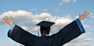 Graduate in cap and gown with arms raised against a blue sky