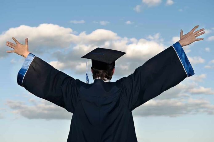 Graduate in cap and gown with arms raised against a blue sky