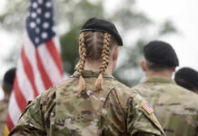 Women Still Proving Themselves in Combat Soldier with braided hair in uniform, American flag visible.