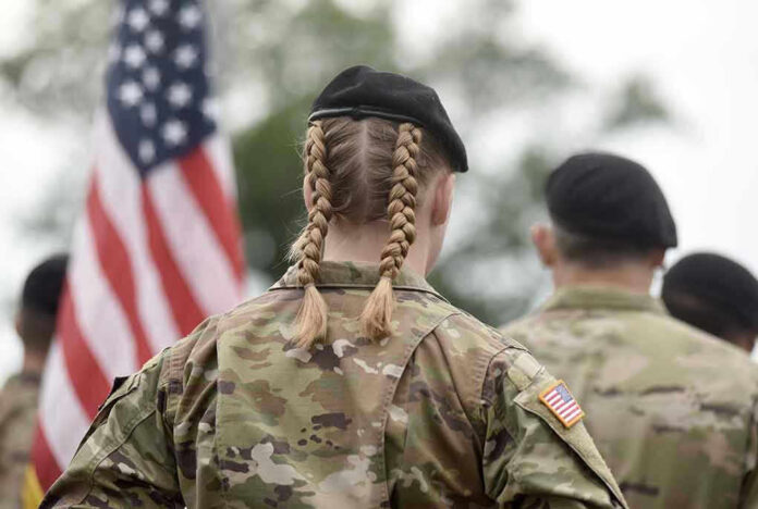 Soldier with braided hair in uniform, American flag visible.