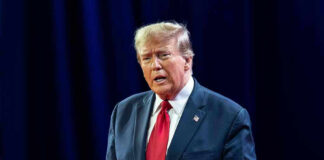 Man in suit with red tie speaking on stage.