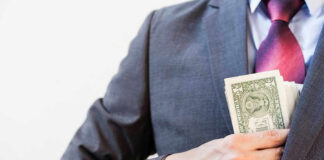 Person in suit putting dollars in jacket pocket.