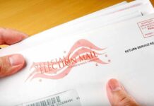 A hand holding an envelope labeled Official Election Mail