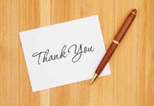 A thank you card with elegant handwriting next to a pen on a wooden table