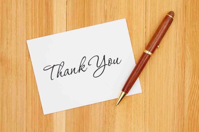 shutterstock_1665640309 (1).jpg A thank you card with elegant handwriting next to a pen on a wooden table