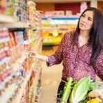 Woman shopping in a grocery store aisle with a cart full of vegetables