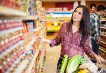 Woman shopping in a grocery store aisle with a cart full of vegetables
