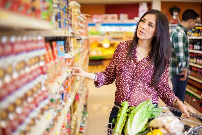 Woman shopping in a grocery store aisle with a cart full of vegetables