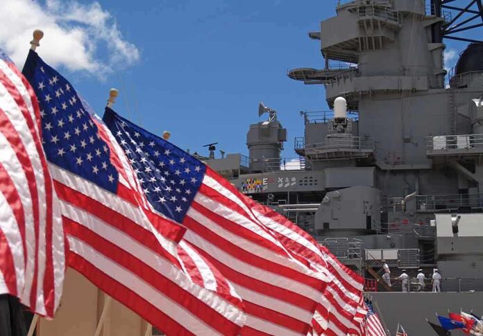 American flags in front of a naval ship under a blue sky