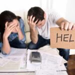 Americans Facing UNPRECEDENTED Midlife Crisis A distressed couple surrounded by paperwork, with one holding a sign that says HELP
