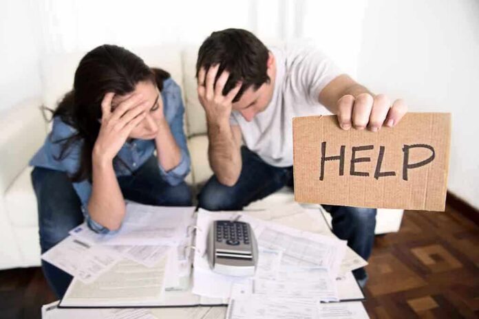 A distressed couple surrounded by paperwork, with one holding a sign that says HELP