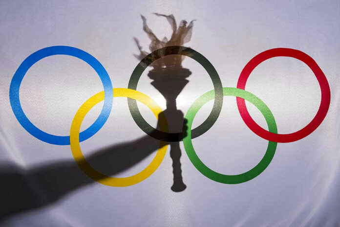 Shadow of torch over Olympic rings logo.