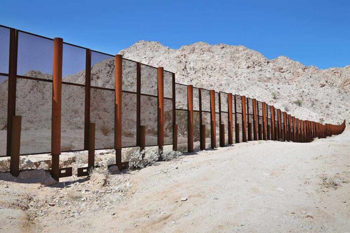A long border wall stretches across a desert landscape with mountains in the background