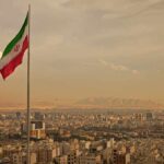 Iranian flag waving over a city skyline with mountains in the background
