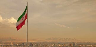 Iranian flag waving over a city skyline with mountains in the background
