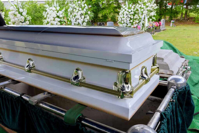White coffin with flowers in the background.