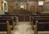 ICE Fills Court: 82 Judges in Blitz Hire! Interior view of an empty courtroom with wooden benches and a judges bench