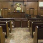 ICE Fills Court: 82 Judges in Blitz Hire! Interior view of an empty courtroom with wooden benches and a judges bench