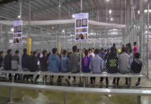 People sitting on benches inside a fenced facility.