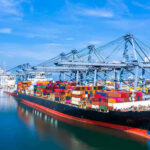 Iran Immediately Shuts Strait AGAIN – They Are Fuming! Container ship docked at a busy industrial port.