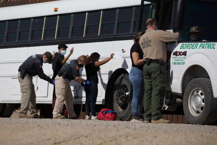 1973414852 Border patrol officers investigating people near a bus.