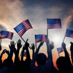 Joy Reid Torches July 4th – Backlash Erupts! Silhouetted crowd holding American flags against a sunset sky