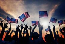 Joy Reid Torches July 4th – Backlash Erupts! Silhouetted crowd holding American flags against a sunset sky