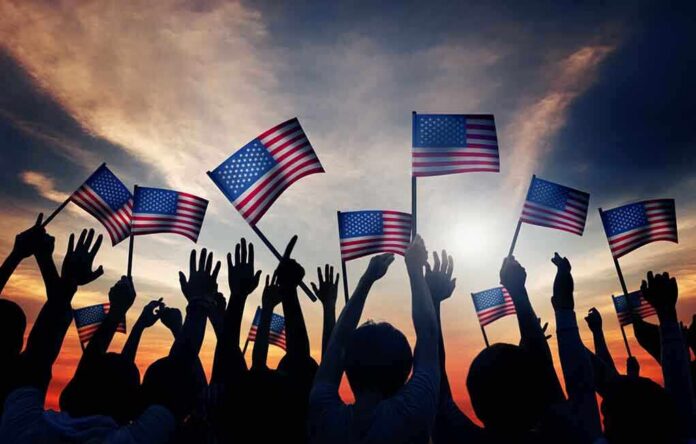 shutterstock_216220174 Silhouetted crowd holding American flags against a sunset sky