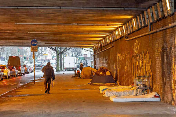 2423598655 People walk under a bridge with homeless encampment.