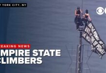 2 climbers unfurl banner at top of Empire State Building.