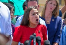 AOC Accent Flip Sparks Firestorm Woman in red dress speaking passionately at outdoor press conference