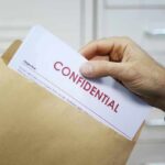 Pentagon on LOCKDOWN After Catastrophic Intel Leak Hand placing confidential document into a brown envelope