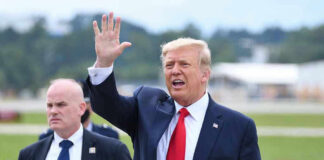 Donald Trump waves while walking outdoors with security nearby