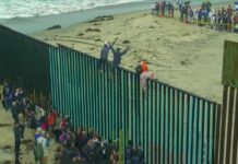 U.S Issues Immediate Travel Warning – Avoid THIS Region! People climbing a tall beachside border fence