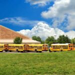 Field Trip Horror – Teacher and Student DEAD! A row of yellow school buses parked in front of a school building under a cloudy sky