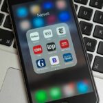 Trump YANKS Billion Dollar Lawsuit Smartphone displaying a folder of news apps on a laptop keyboard
