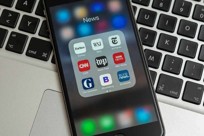 shutterstock_1321128134 Smartphone displaying a folder of news apps on a laptop keyboard