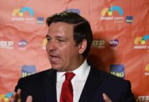 DeSantis Sounds Alarm: Institutions On The Chopping Block Man in a suit speaking at a media backdrop