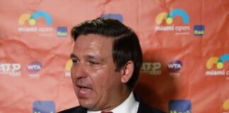 Man in a suit speaking at a media backdrop