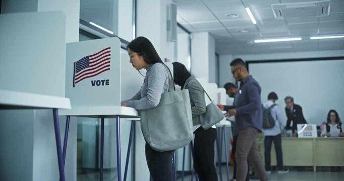 shutterstock_2451104741 Voters at polling booths in a modern voting center