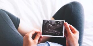 Person holding an ultrasound photo over a pregnant belly