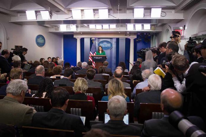shutterstock_744405130 Press secretary at podium addressing reporters in briefing room