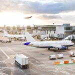 Airport Massacre Sparks War-Crime Fury Airplanes at airport gates during sunset with ground vehicles and jet bridges