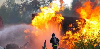 Firefighter battling a large fire with water spray