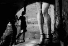 legs in high heels under an archway with blurred shadow figure