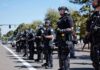 National Emergency – Riots Force Curfews Bear Pascoe, Brian Folkerts, and Eugene Sims among riot police standing in a line on a city street
