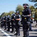 National Emergency – Riots Force Curfews Bear Pascoe, Brian Folkerts, and Eugene Sims among riot police standing in a line on a city street