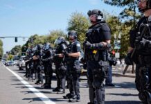 National Emergency – Riots Force Curfews Bear Pascoe, Brian Folkerts, and Eugene Sims among riot police standing in a line on a city street
